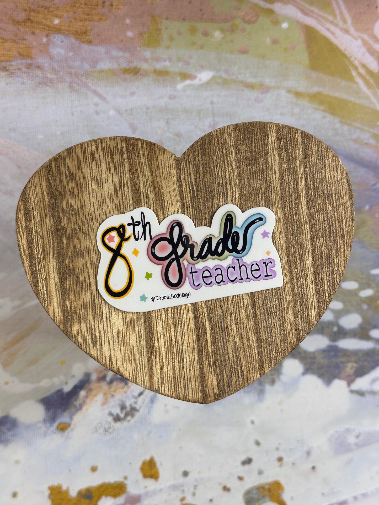 8th Grade teacher vinyl sticker on a wooden heart-shaped table with colorful background, showing bold cute font with colorful letter highlights.