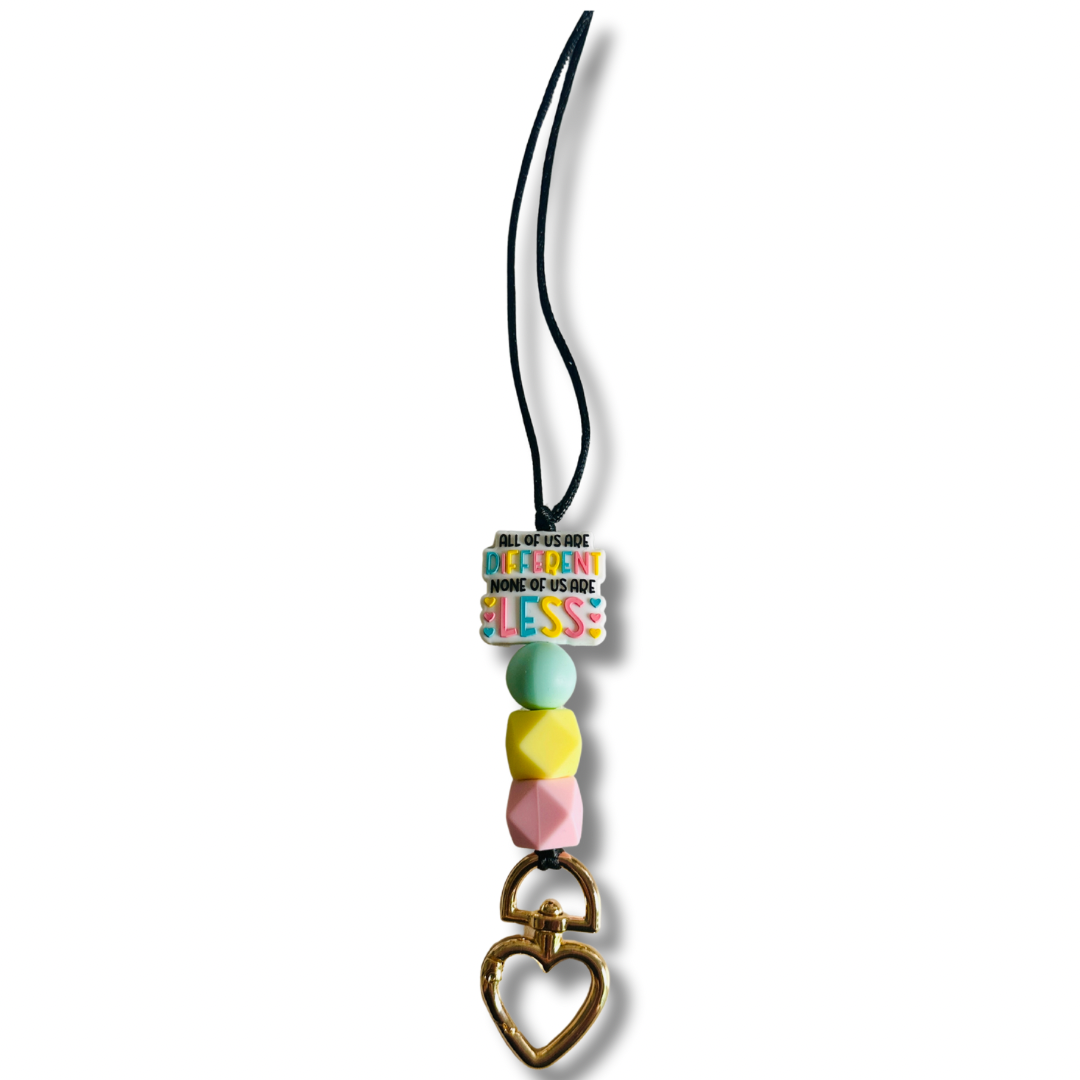 Black nylon teacher lanyard featuring the inspiring message "All of us are different. None of us are less" with colorful pink, yellow, and light blue silicone accents, breakaway clasp, and heart-shaped metal badge clip.