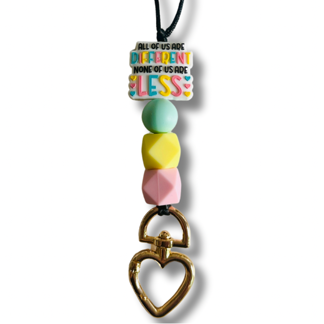 Black nylon teacher lanyard featuring the inspiring message "All of us are different. None of us are less" with colorful pink, yellow, and light blue silicone accents, breakaway clasp, and heart-shaped metal badge clip.