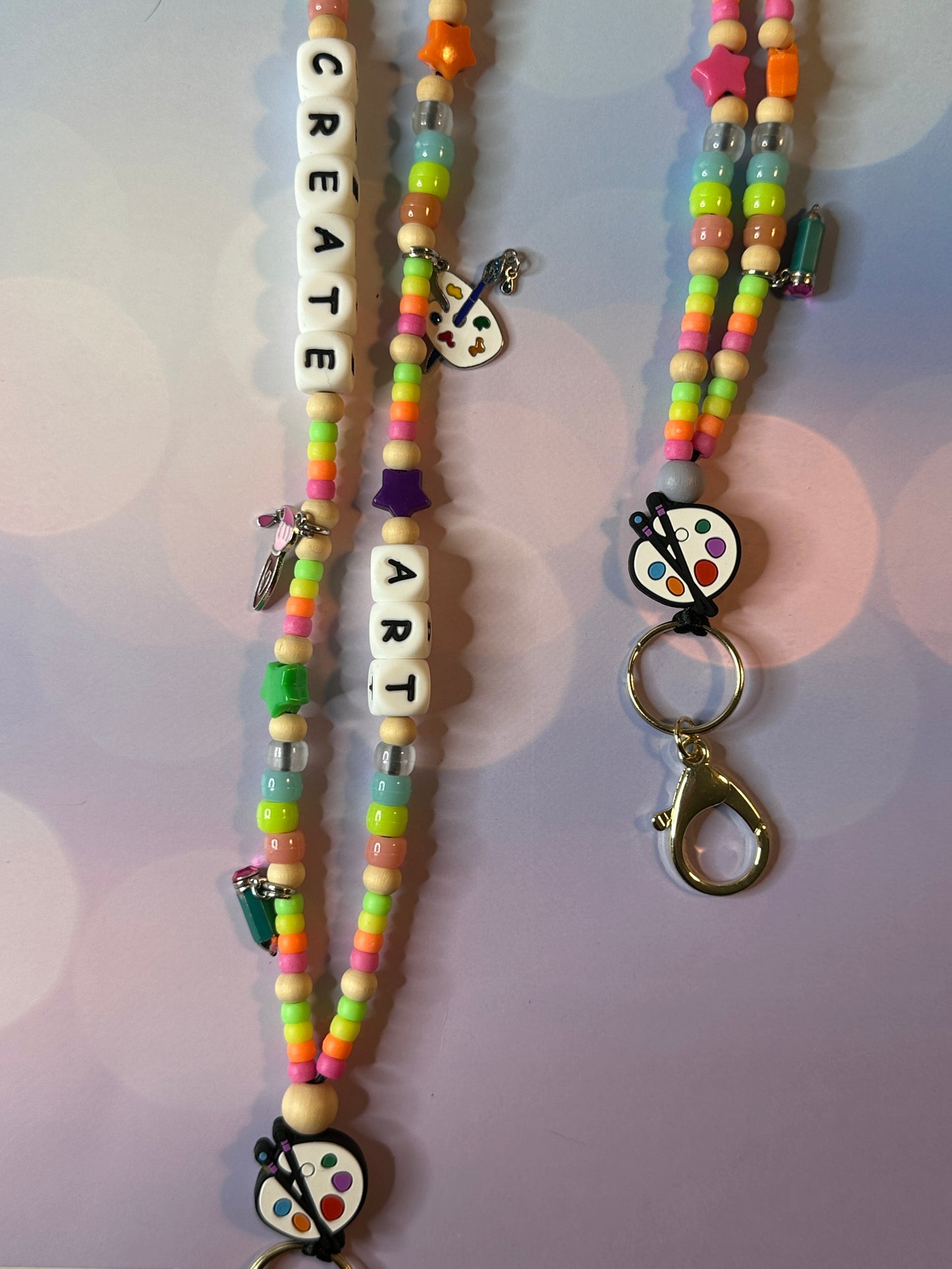 Two art teacher lanyards. One lanyard is displaying the charms and colorful beads and the other is displaying the metal clasp.