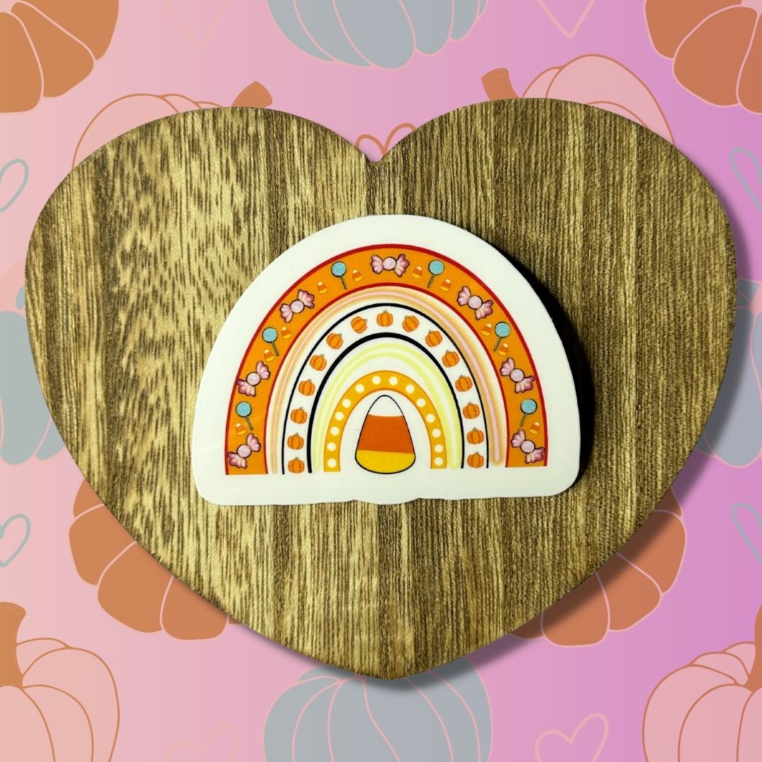 Candy corn rainbow waterproof vinyl sticker with pumpkins, lollipops, and candy corns on heart-shaped wooden table with colorful background.