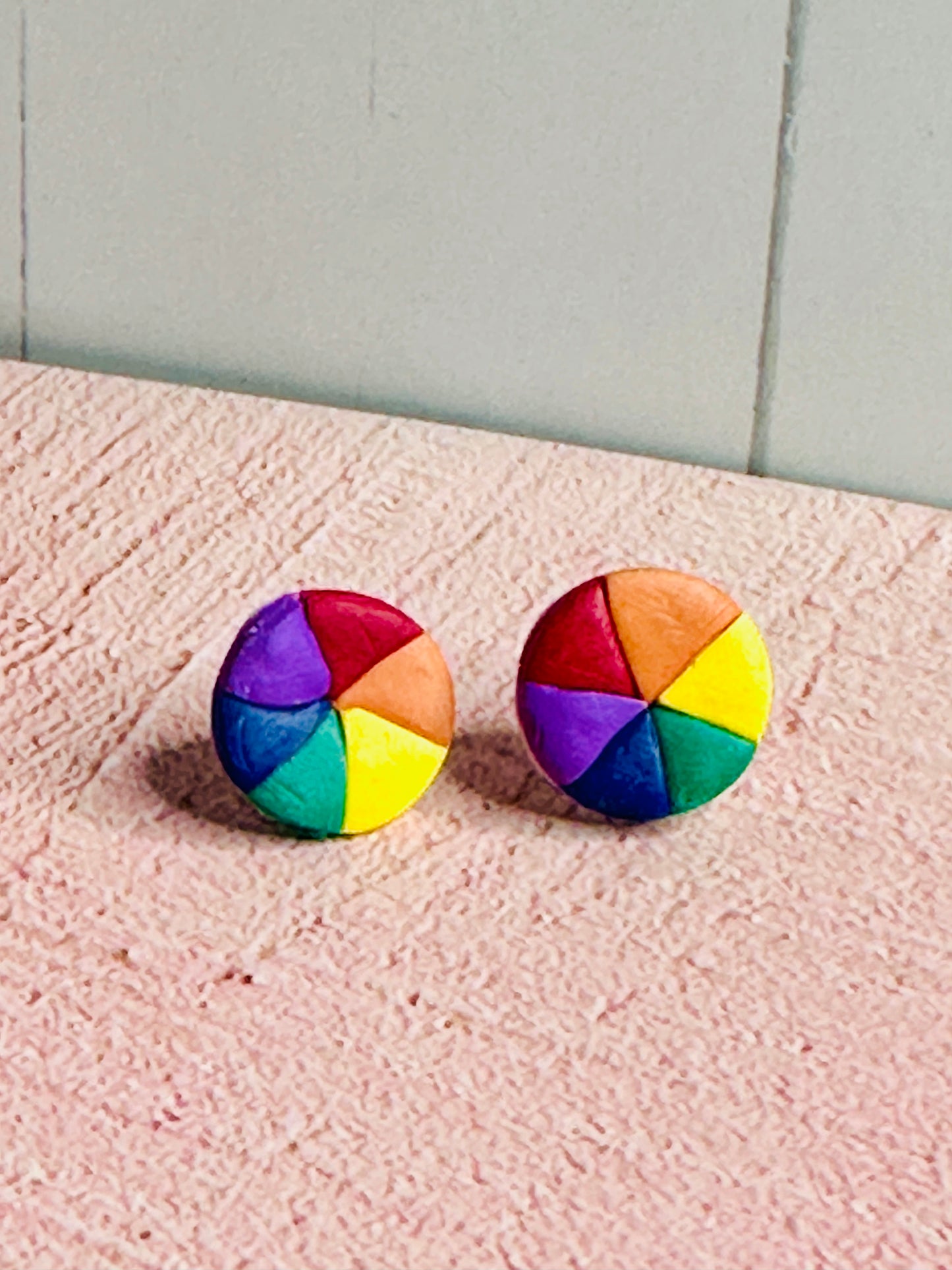 Zoomed-out view of Color Wheel Stud Earrings displayed on pink table surface showing full earring size and proportions.