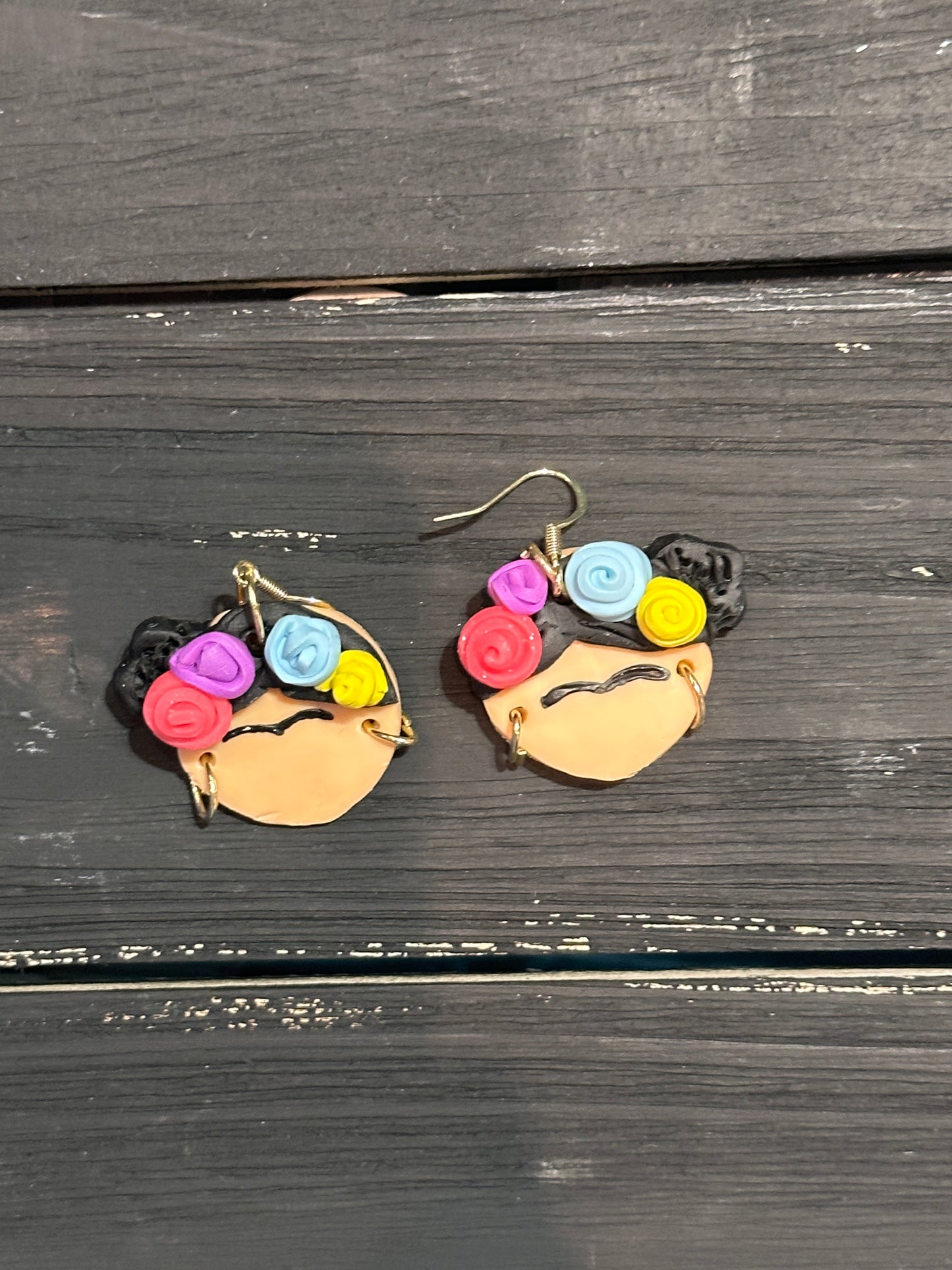 A straight view of the Frida Kahlo earrings sitting on a black wooden table.