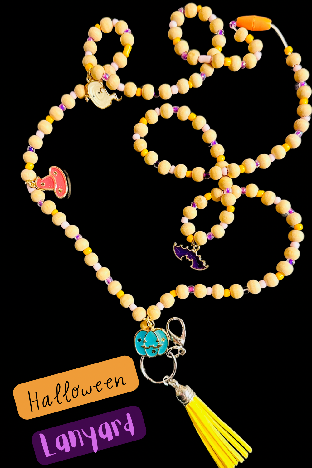 The Halloween Lanyard on a black background. The full lanyard can be seen with its wooden beads, metal charms shaped like pumpkins, bats, witch hats, and ghosts, and colorful tassel.