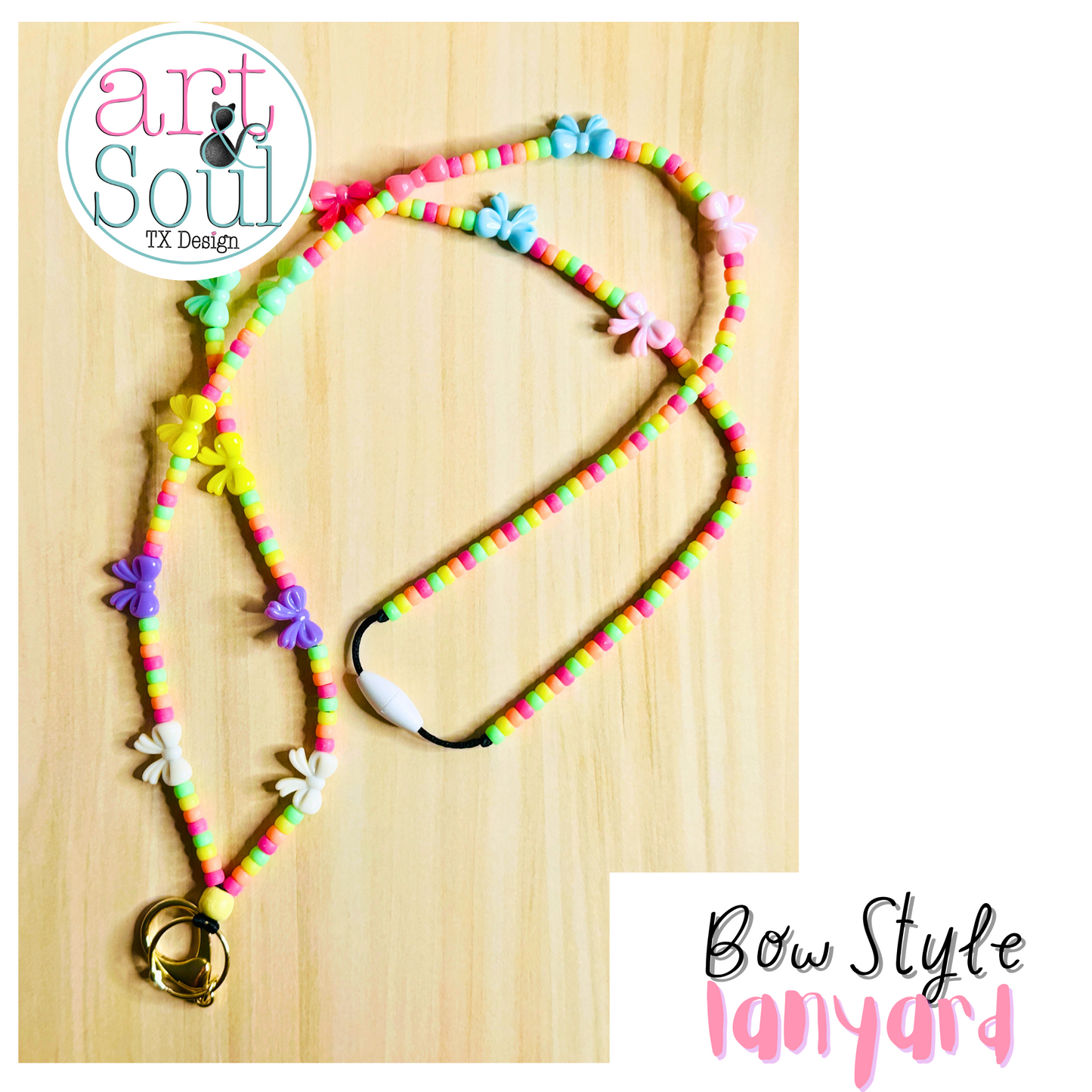 The Mini Bow Lanyard on a wooden table. The rainbow colored beads, bows, keychain, and breakaway clasp can be seen.