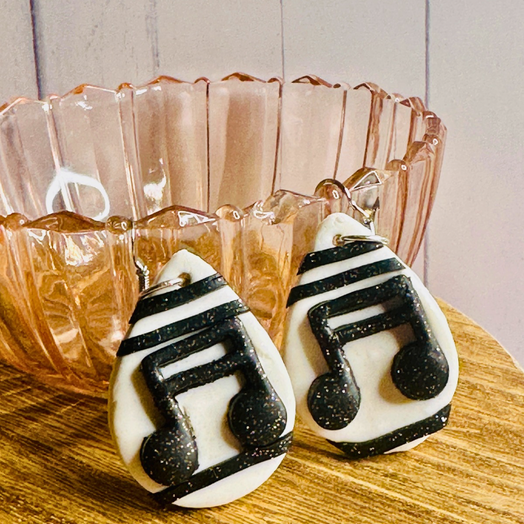 A close up angled shot of the Musical Note Clay Earrings resting against a pink glass bowl.
