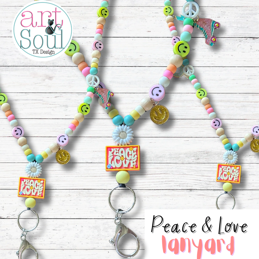 A trio of Peace And Love lanyards on a white wooden backdrop. The silicon Peace and Love sign, metal roller skate and smiley face charms, and pastel colored beads and happy faces can be seen.