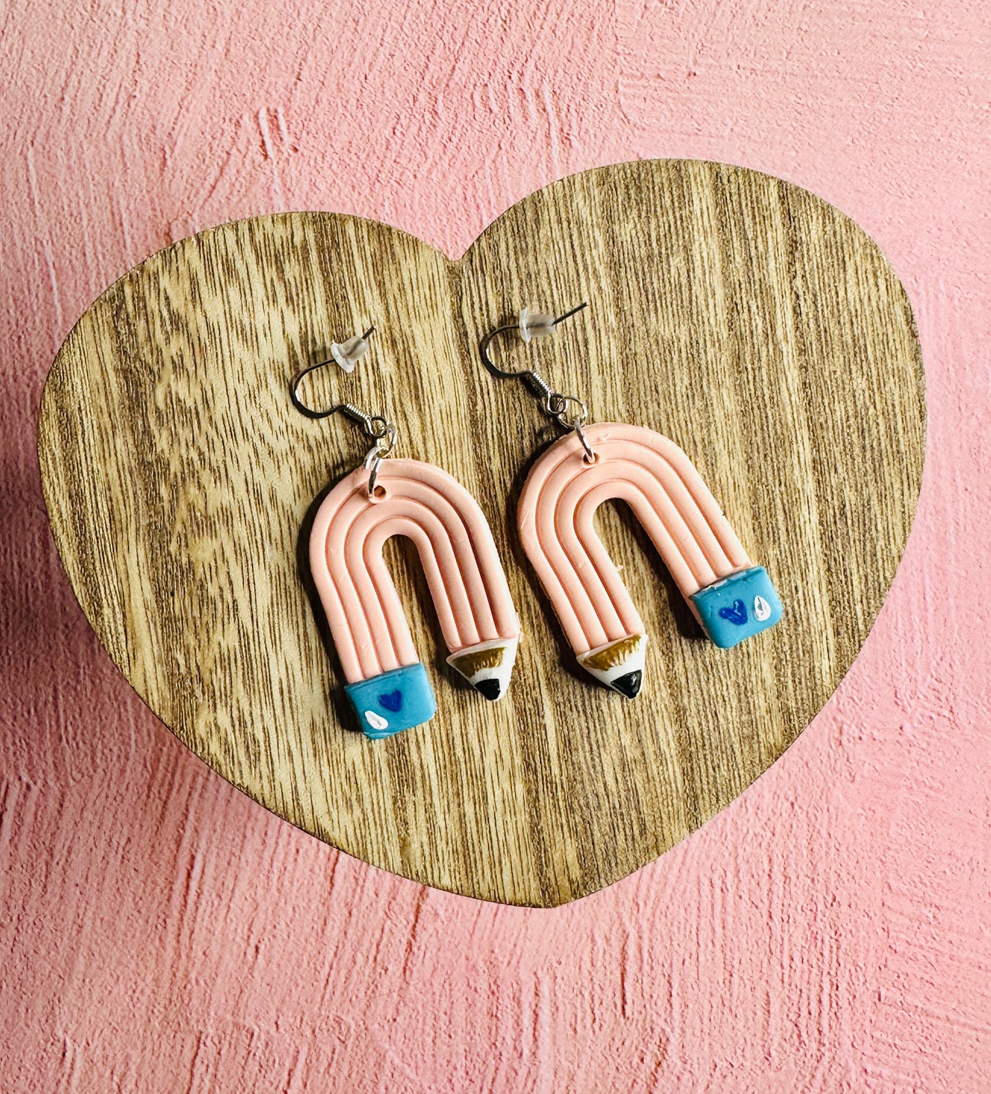 A set of pink pencil teacher earrings on a wooden table shaped like a heart.
