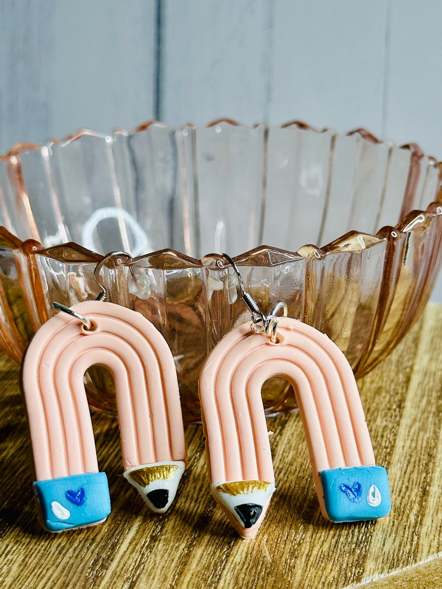 A pair of pink pencil teacher earrings resting against a glass bowl.