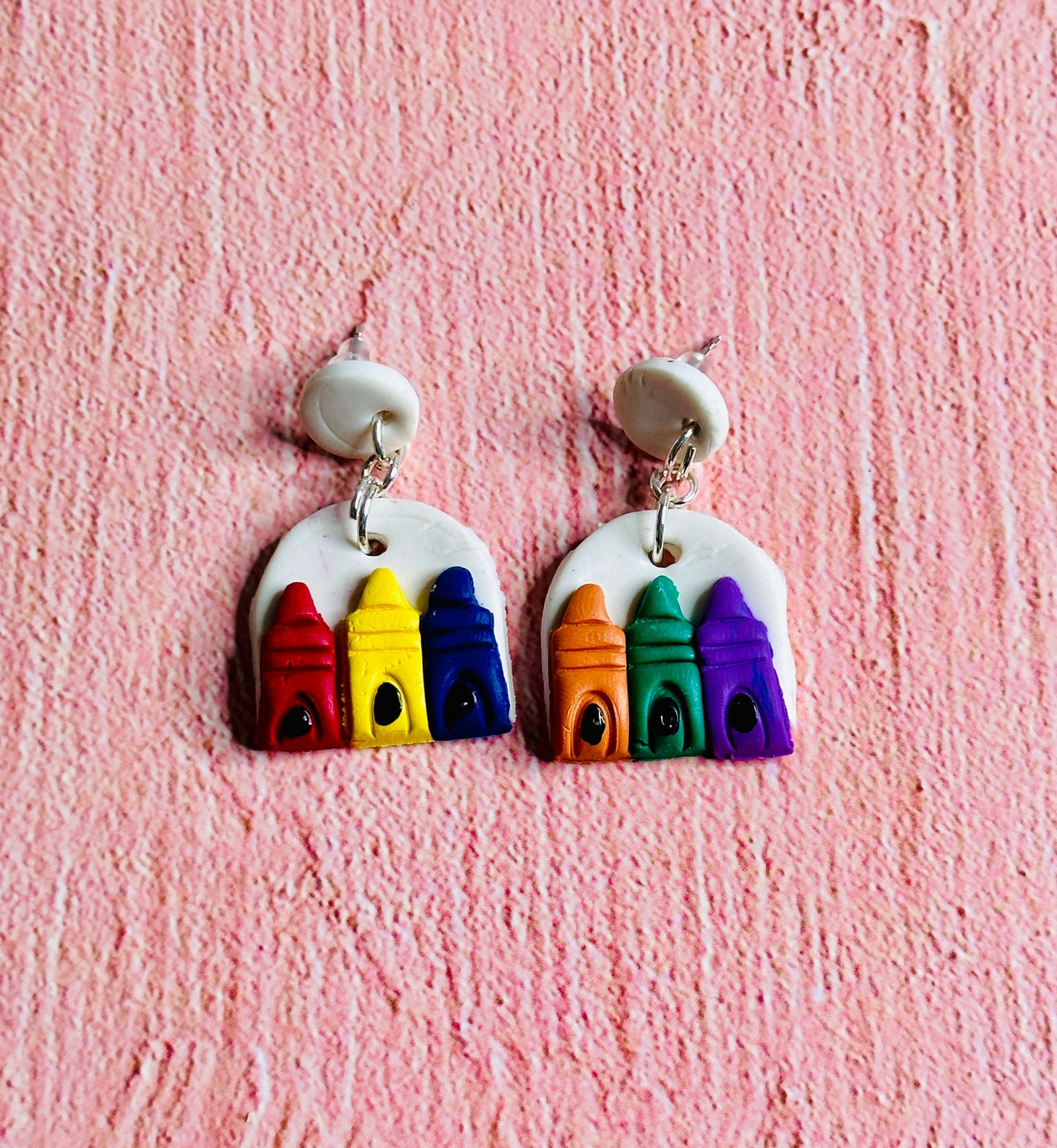 The Primary Color Earring is on the left, with red blue , and yellow crayons on a white background. The Secondary Color Earring is on the right with orange green, and purple crayons on a white background.