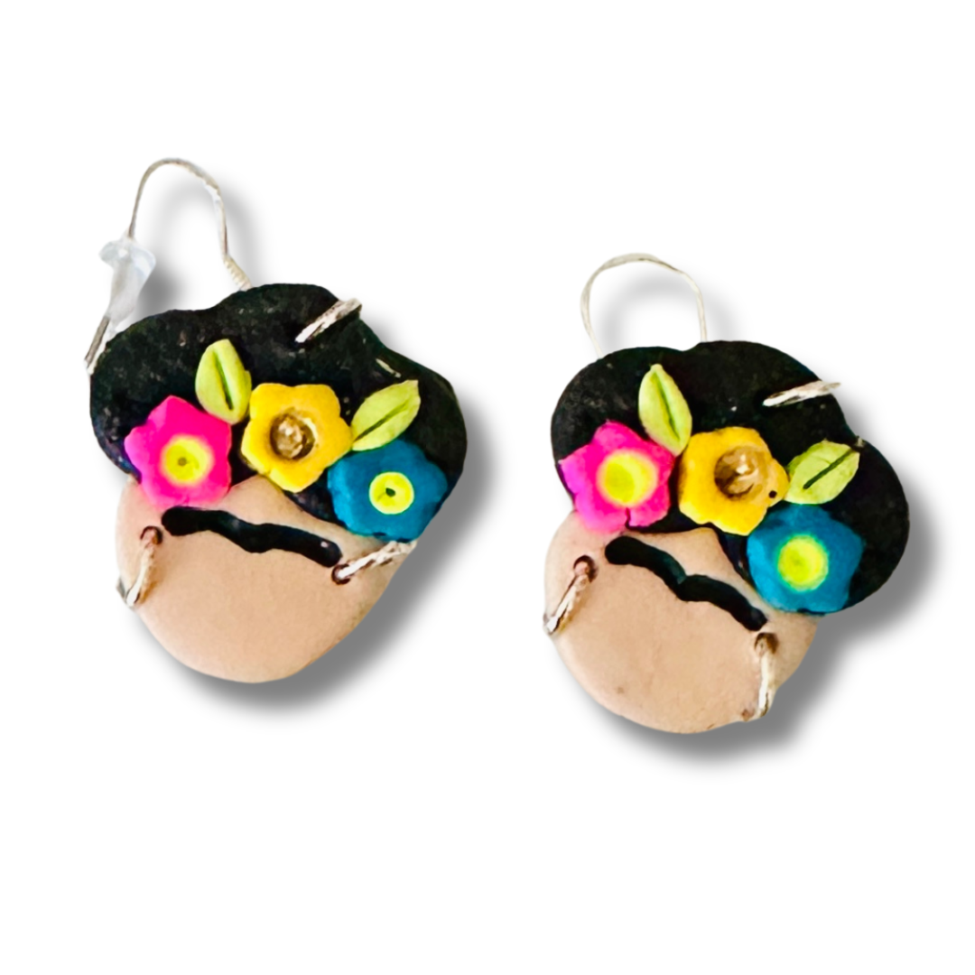 Frida Kahlo-themed earrings with a clean face (no red lips), pink, blue, and yellow flowers adorning her hair, with nickel free loops and hooks on a white background.