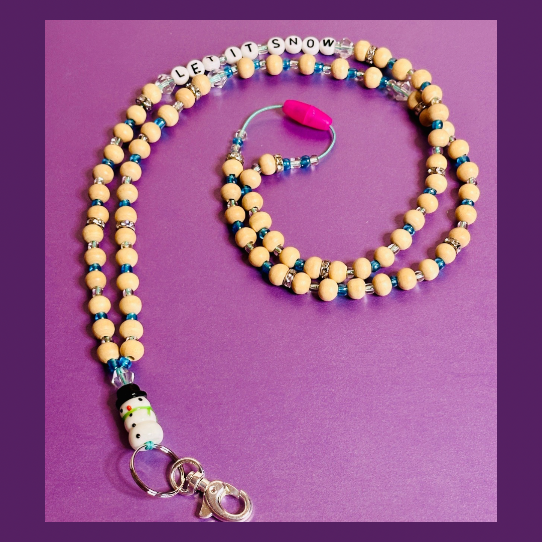 The full Snowman Christmas Lanyard seen from an angle. The lanyard is in a spiral shape with the Snowman charm on the bottom left, the pink breakaway clasp in the middle, and the beaded words "LET IT SNOW" on the top of the image.