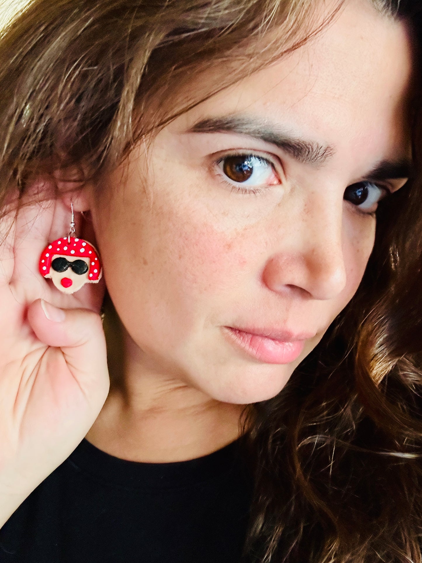 Woman wearing Yayoi Kusama polymer clay earrings displaying the portrait earring with red polka dot hair, black sunglasses and red lips.