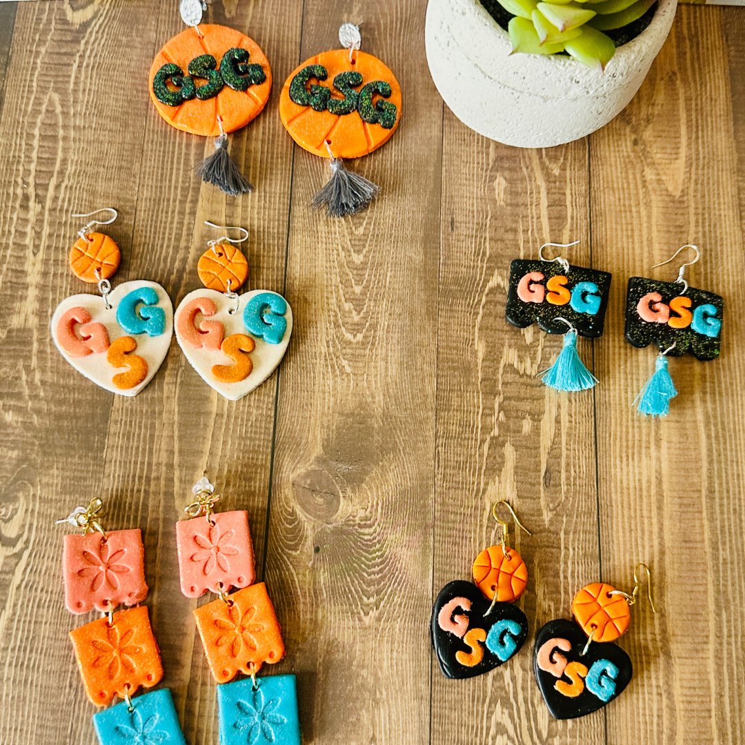 The full Go Spurs Go polymer clay earring collection on a wooden table.