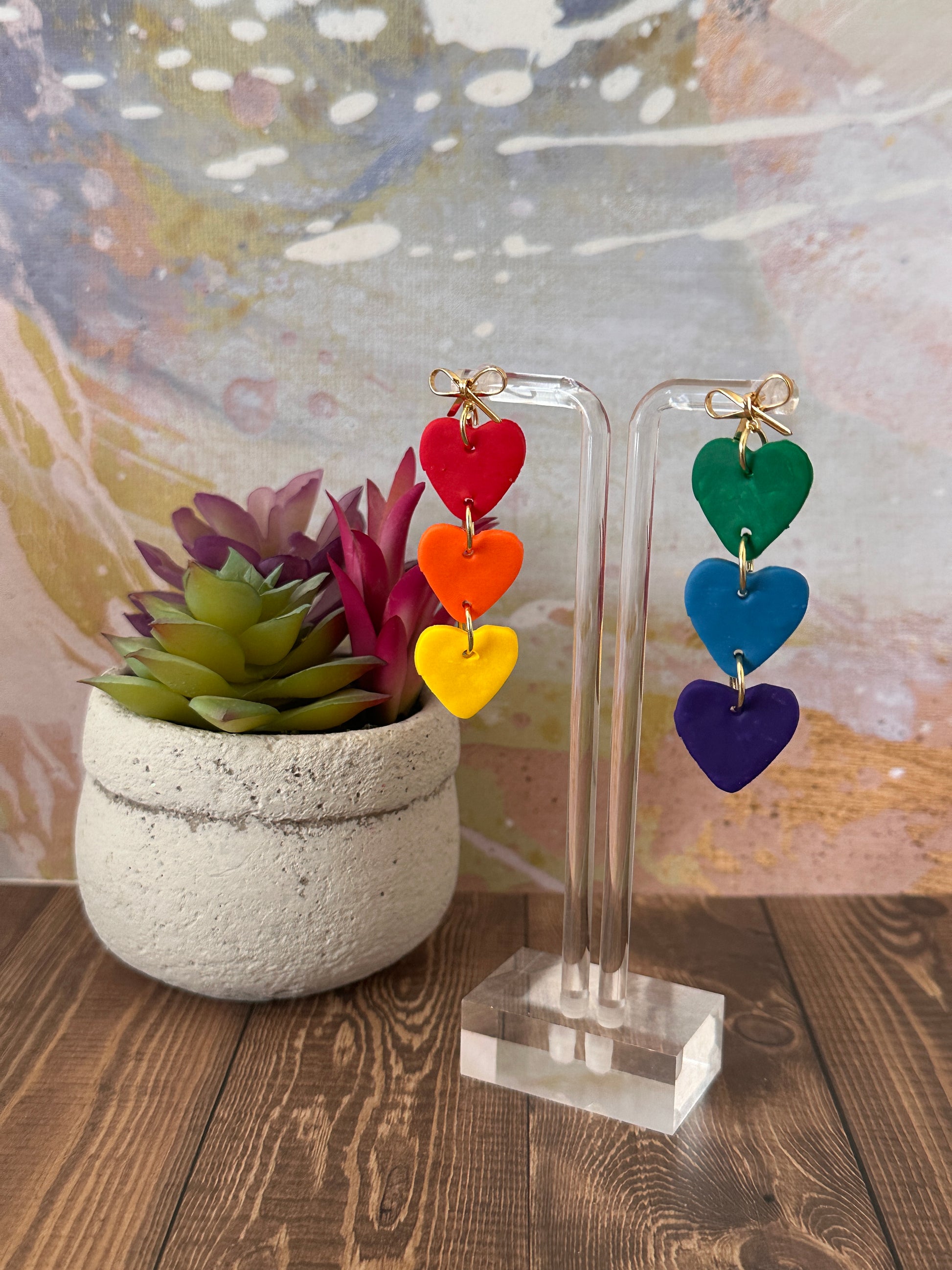 Colorful heart-shaped earrings on a clear stand with a blurred background