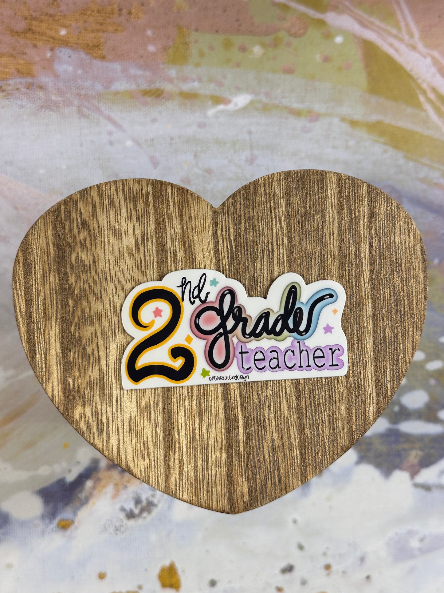 2nd Grade teacher vinyl sticker on a wooden heart-shaped table with colorful background, showing bold cute font with colorful letter highlights.