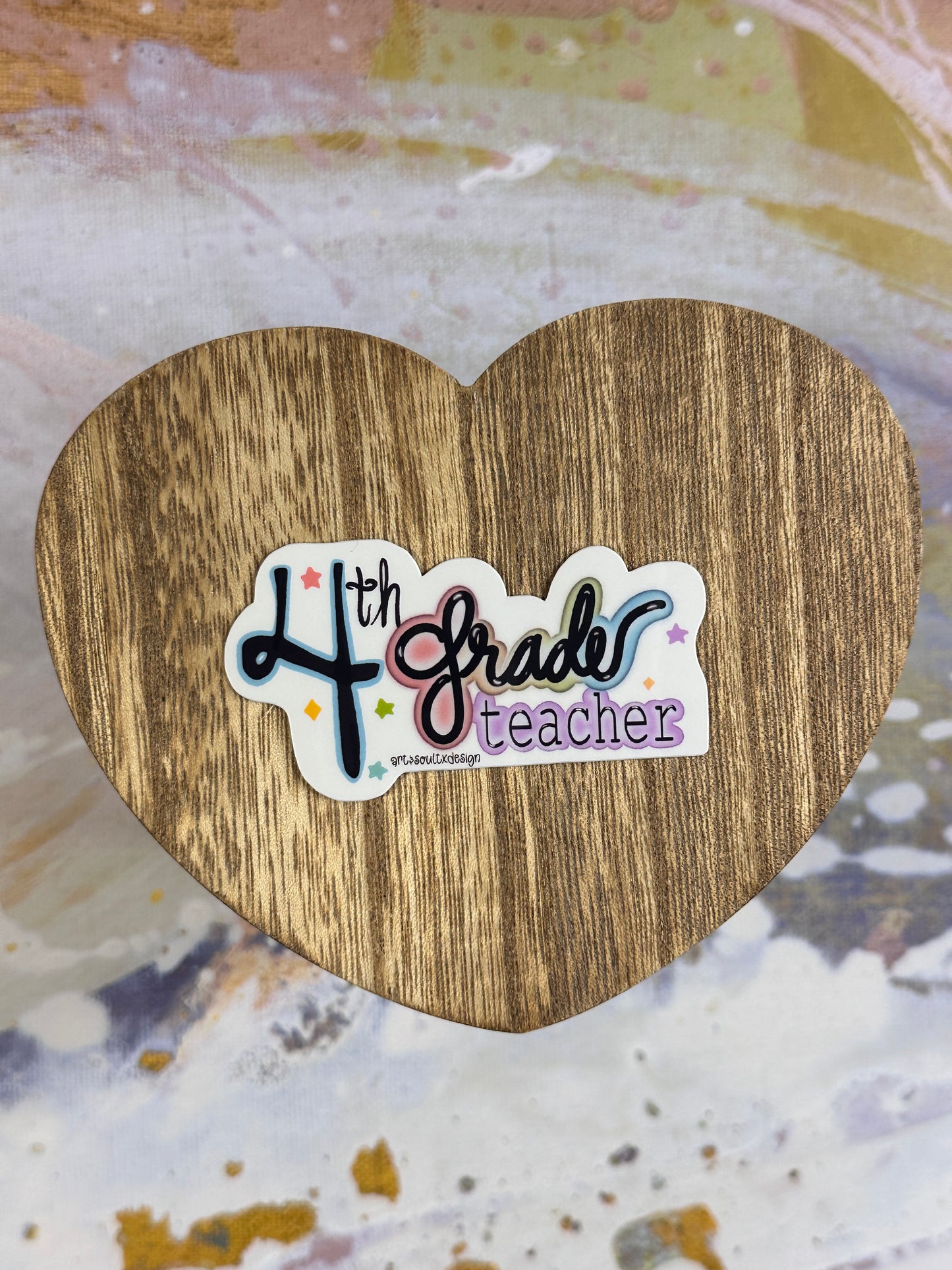 4th Grade teacher vinyl sticker on a wooden heart-shaped table with colorful background, showing bold cute font with colorful letter highlights.