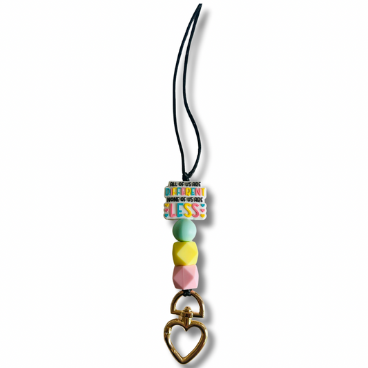 Black nylon teacher lanyard featuring the inspiring message "All of us are different. None of us are less" with colorful pink, yellow, and light blue silicone accents, breakaway clasp, and heart-shaped metal badge clip.