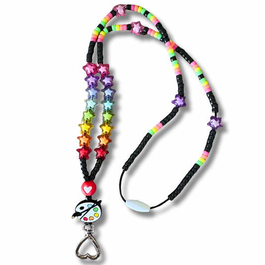 Overhead view of colorful art teacher lanyard with paint palette bead and star beads on white background.