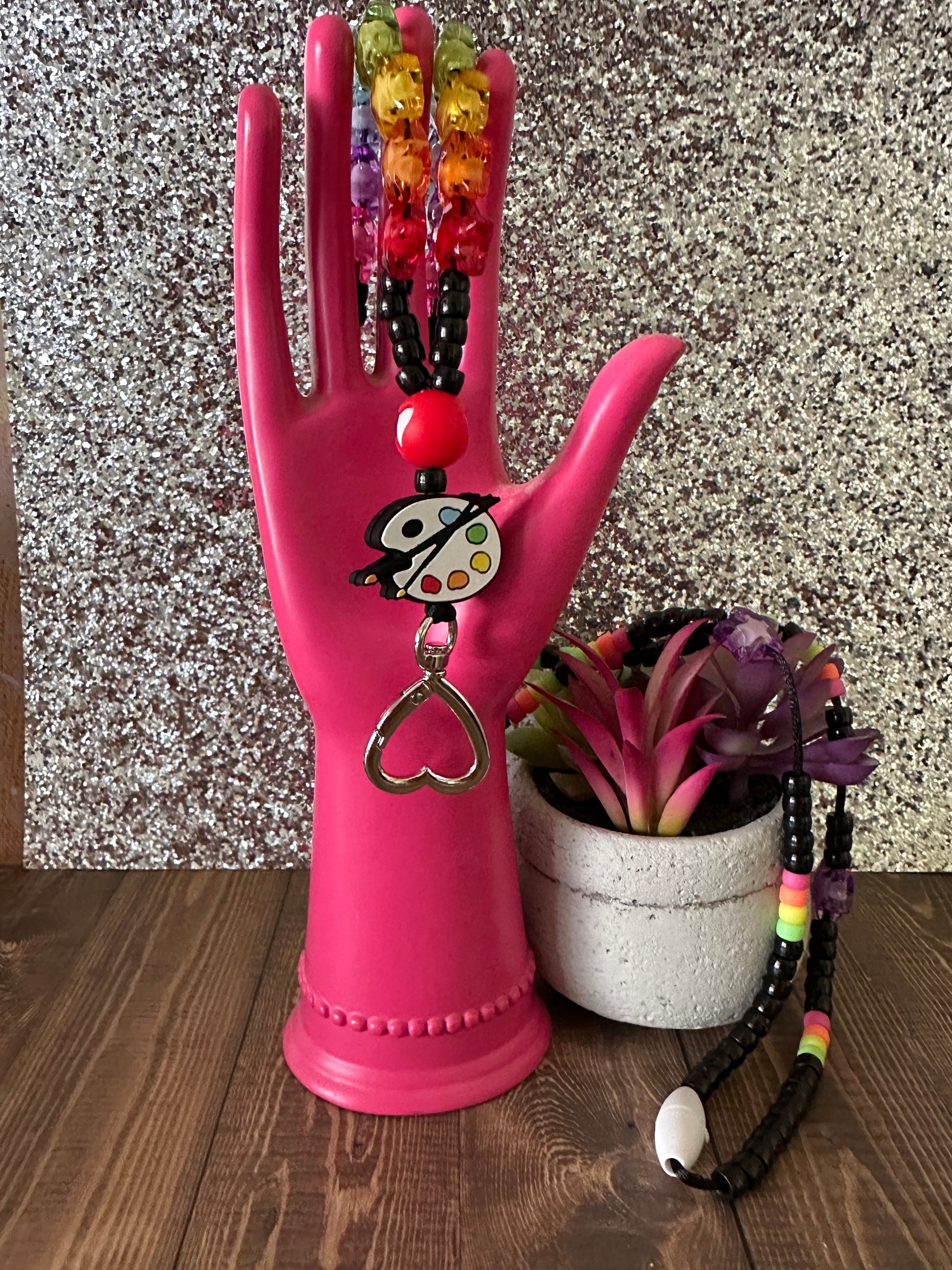  Pink hand statue holding colorful art teacher lanyard against shiny silver background.