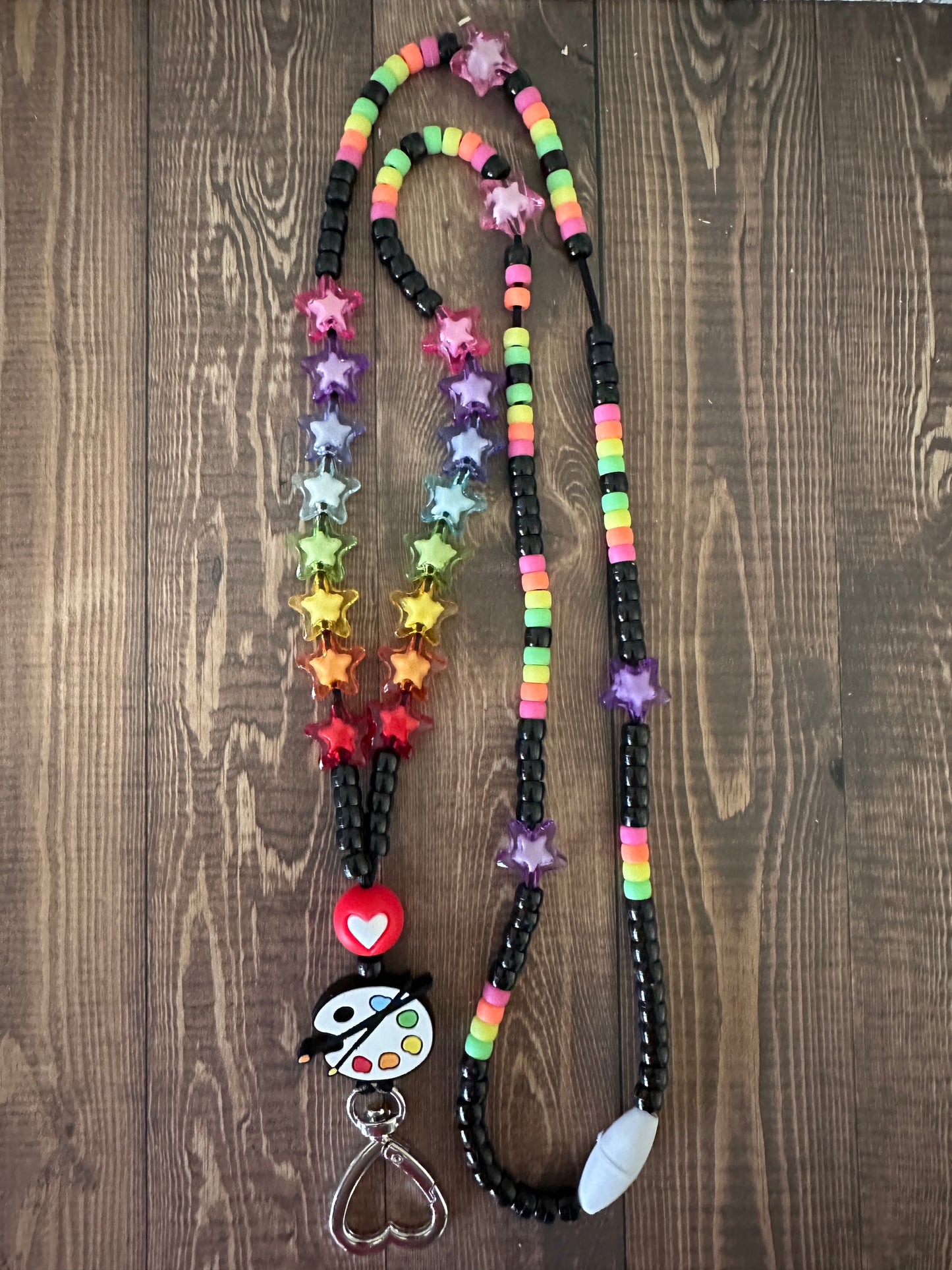 Vibrant art teacher lanyard with paint palette and colorful beads on dark wooden table