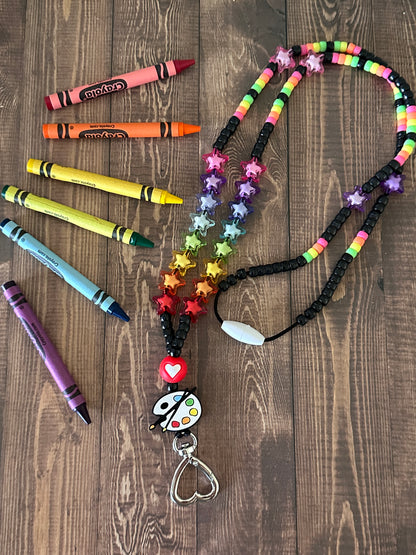 Art teacher lanyard on wooden table with rainbow crayons emphasizing educational art theme