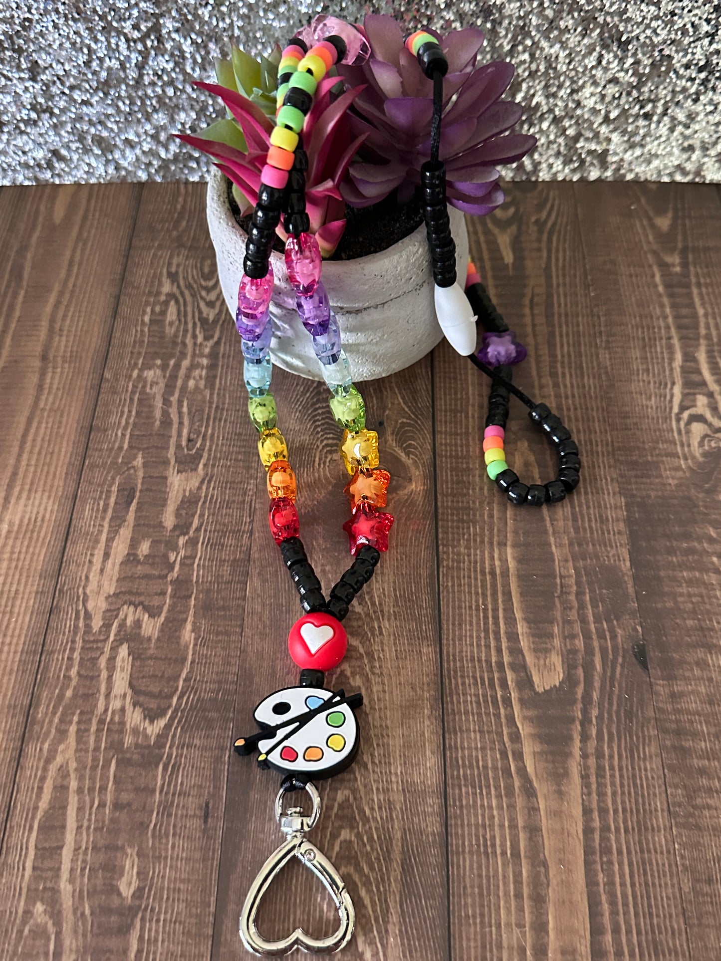 Colorful art teacher lanyard draped over small potted succulent on wooden table.