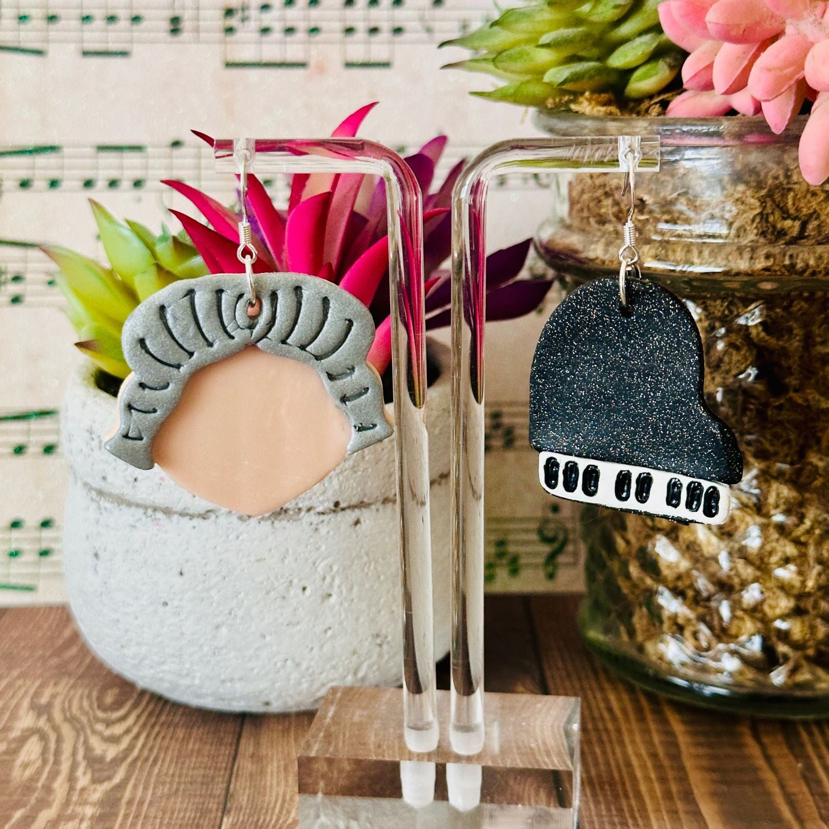 Two pairs of earrings on clear stands with a decorative background