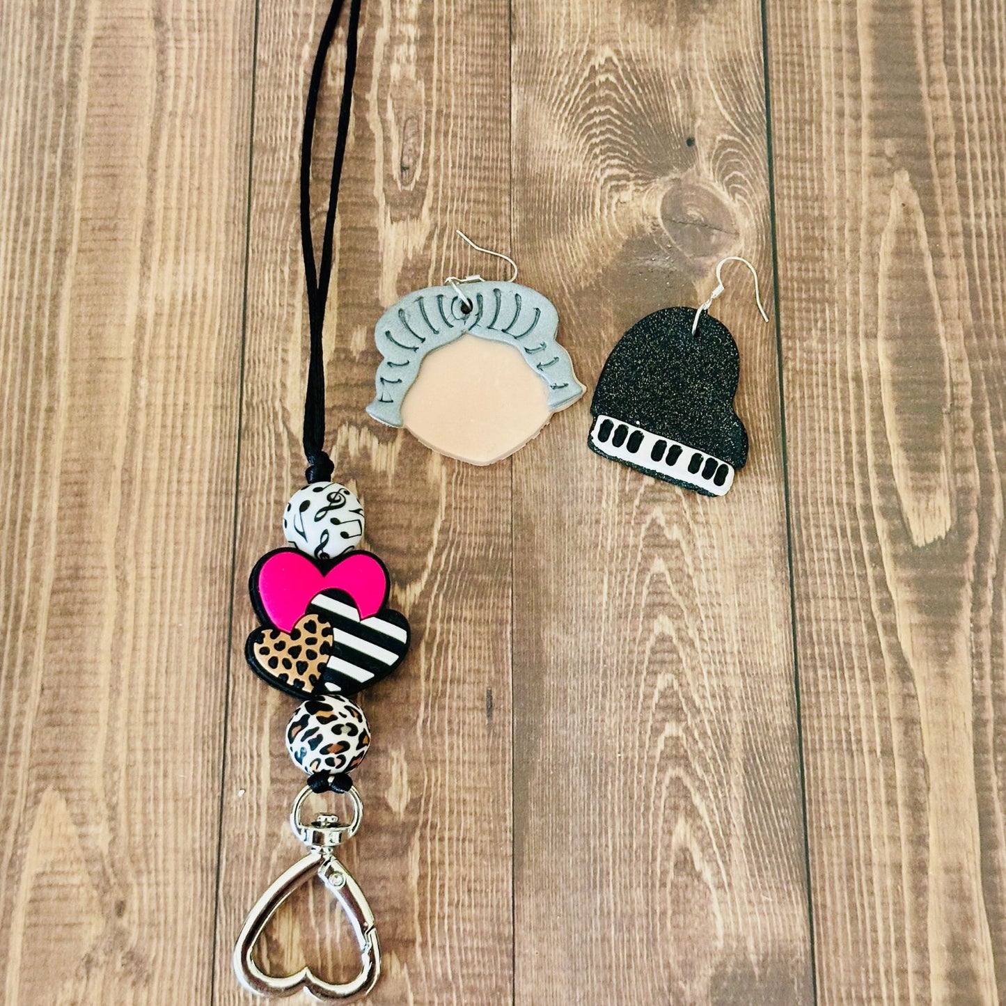 Decorative keychain with heart and animal print design on a wooden surface and beside it are a pair of earrings.