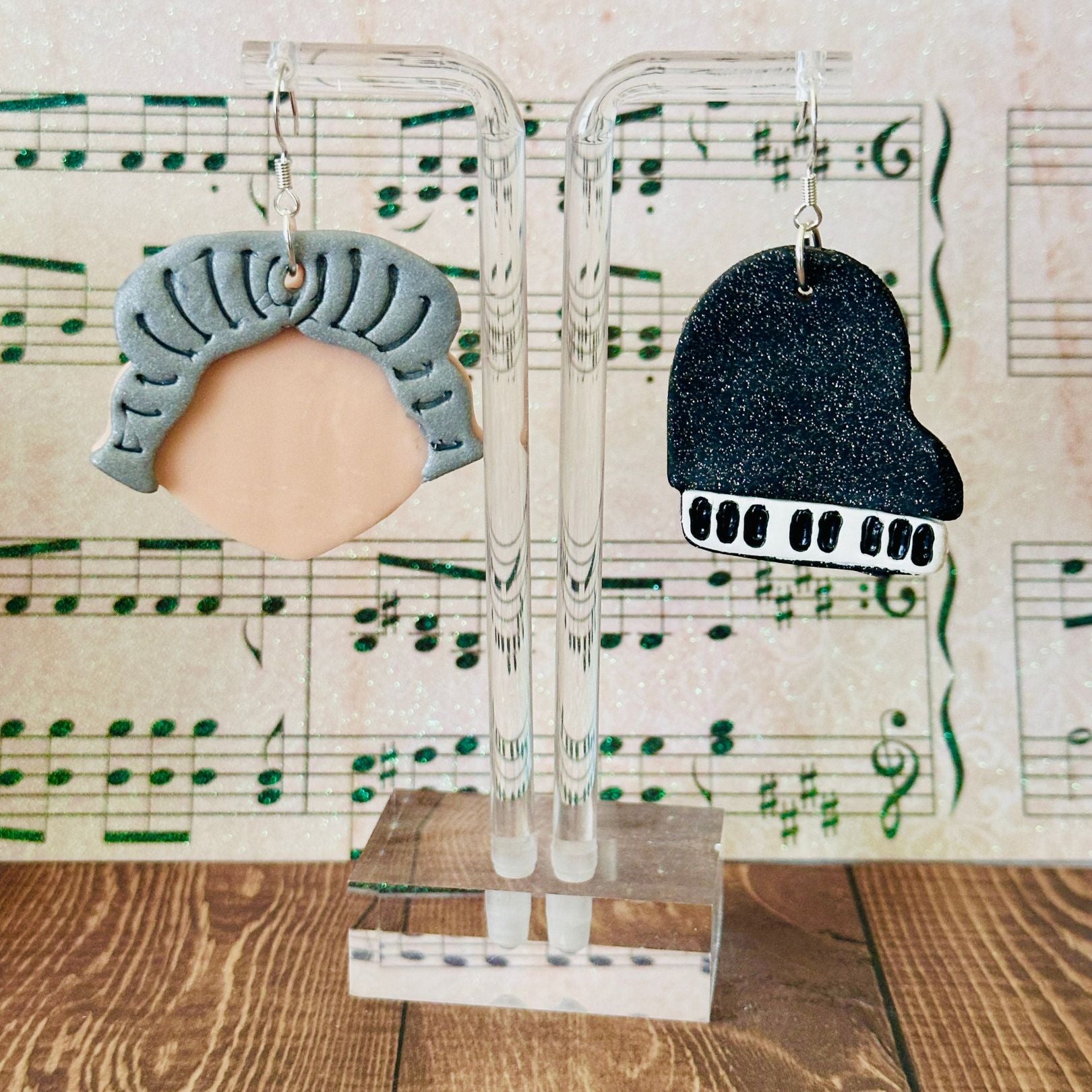 Two pairs of earrings on clear stands with a musical sheet background