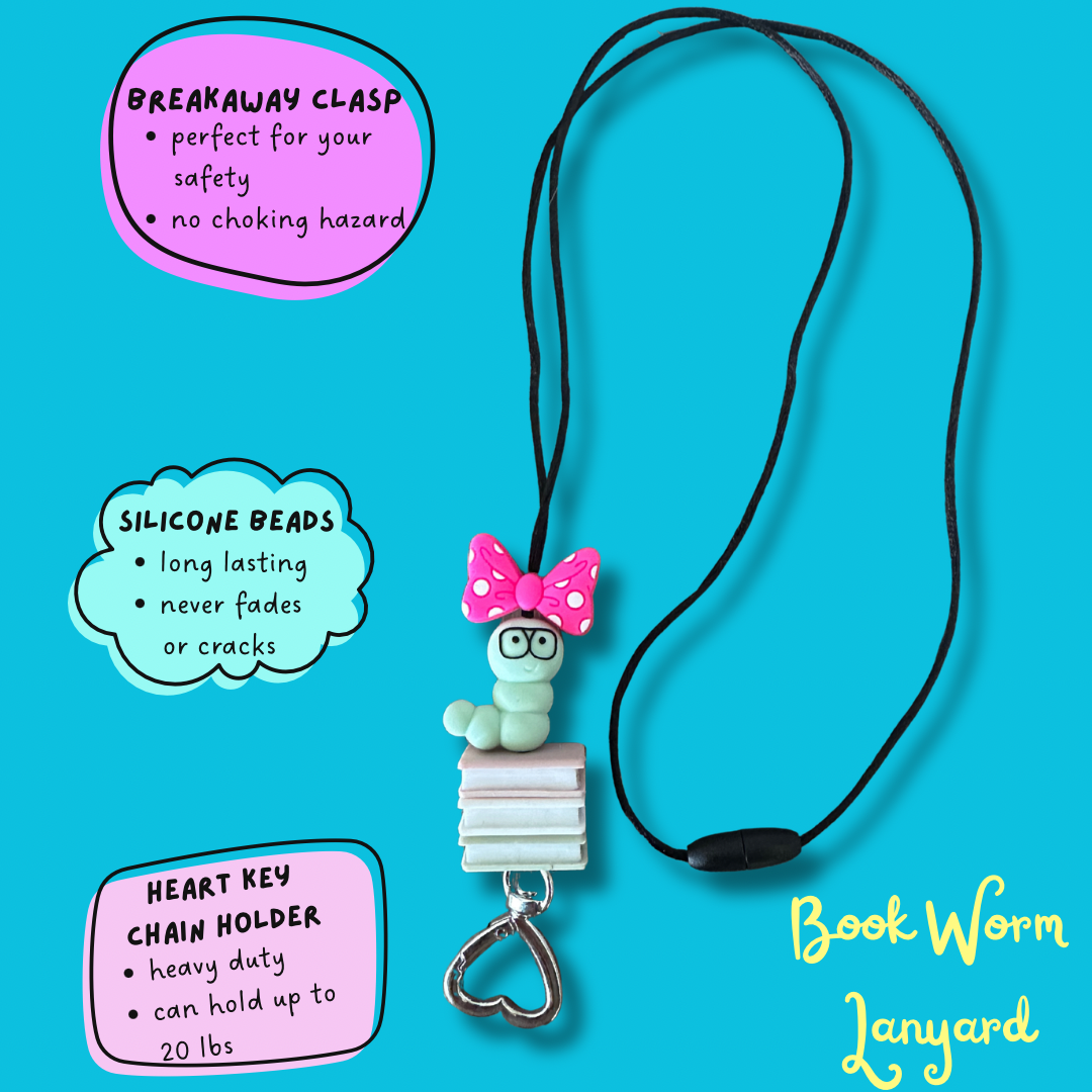 A book worm charm necklace on a black cord, displayed on a bright blue background with three feature callout bubbles and the text 'Book Worm Lanyard'. The necklace features a light green bookworm figure sitting on pink and white books, wearing a pink polka dot bow, and attached to a silver heart-shaped key chain.