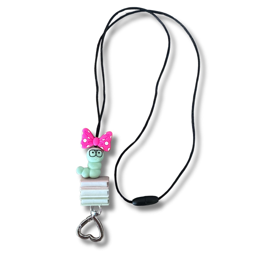 Lanyard on White background showing the close up of silicone beaded pink bow, green worm, pink book, white book, and green book. 