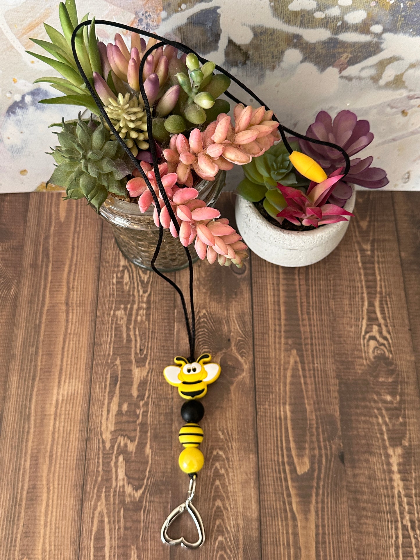 Bumble Bee Teacher Lanyard Full View
Alt Text: Bumble bee beaded lanyard with safety breakaway clasp and heart key holder draped over succulents on wood table.