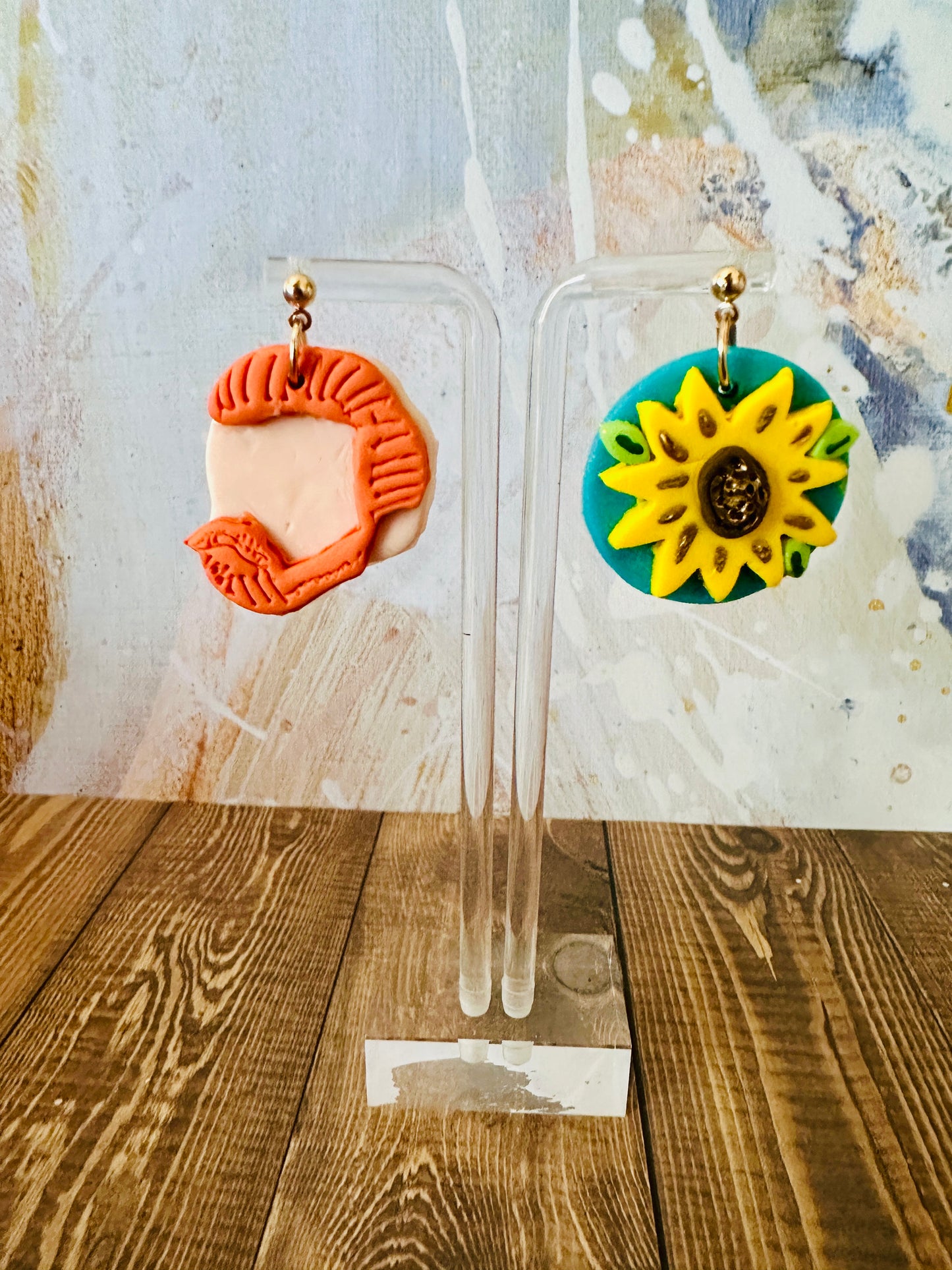 Close up of handcrafted Van Gogh sunflower earrings hanging on stand with wooden table and vibrant colorful background.