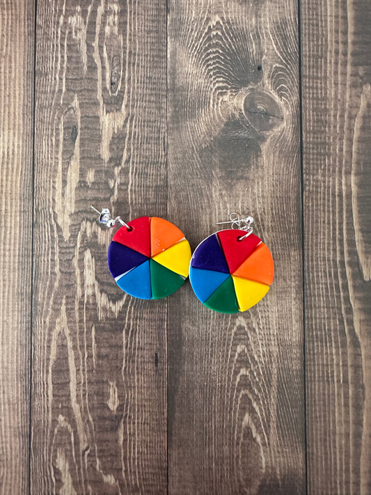 Handmade color wheel polymer clay earrings displayed on a wooden surface, showing vibrant hand-painted color wheel design.