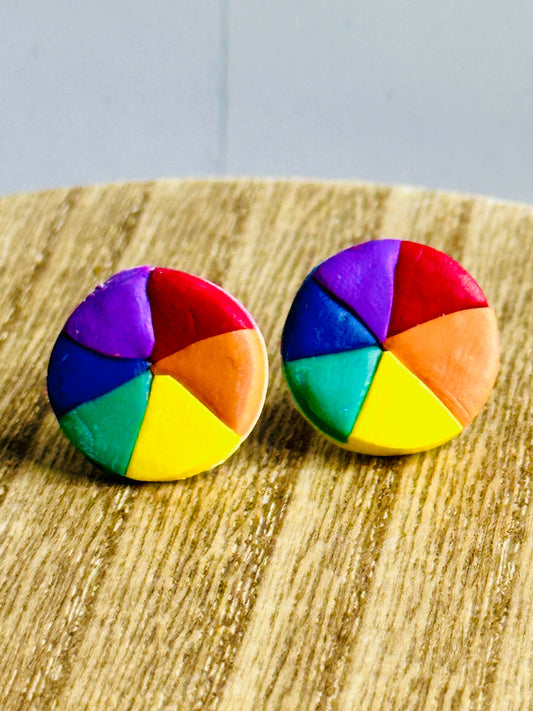 Close-up view of Color Wheel Stud Earrings on wooden table showing detailed polymer clay color wheel design with primary and secondary colors.