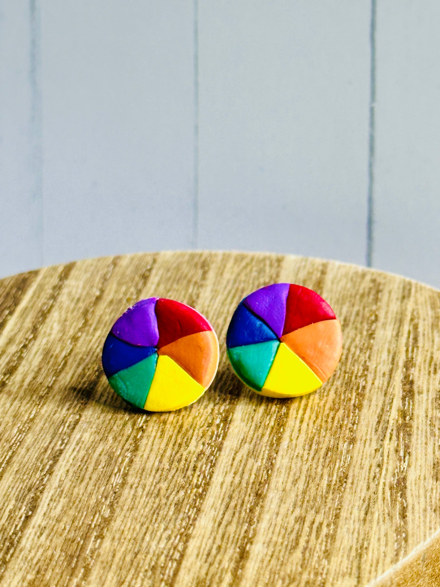 A pair of polymer clay earrings shaped like color wheels for artists and art teachers sitting on a wooden table.