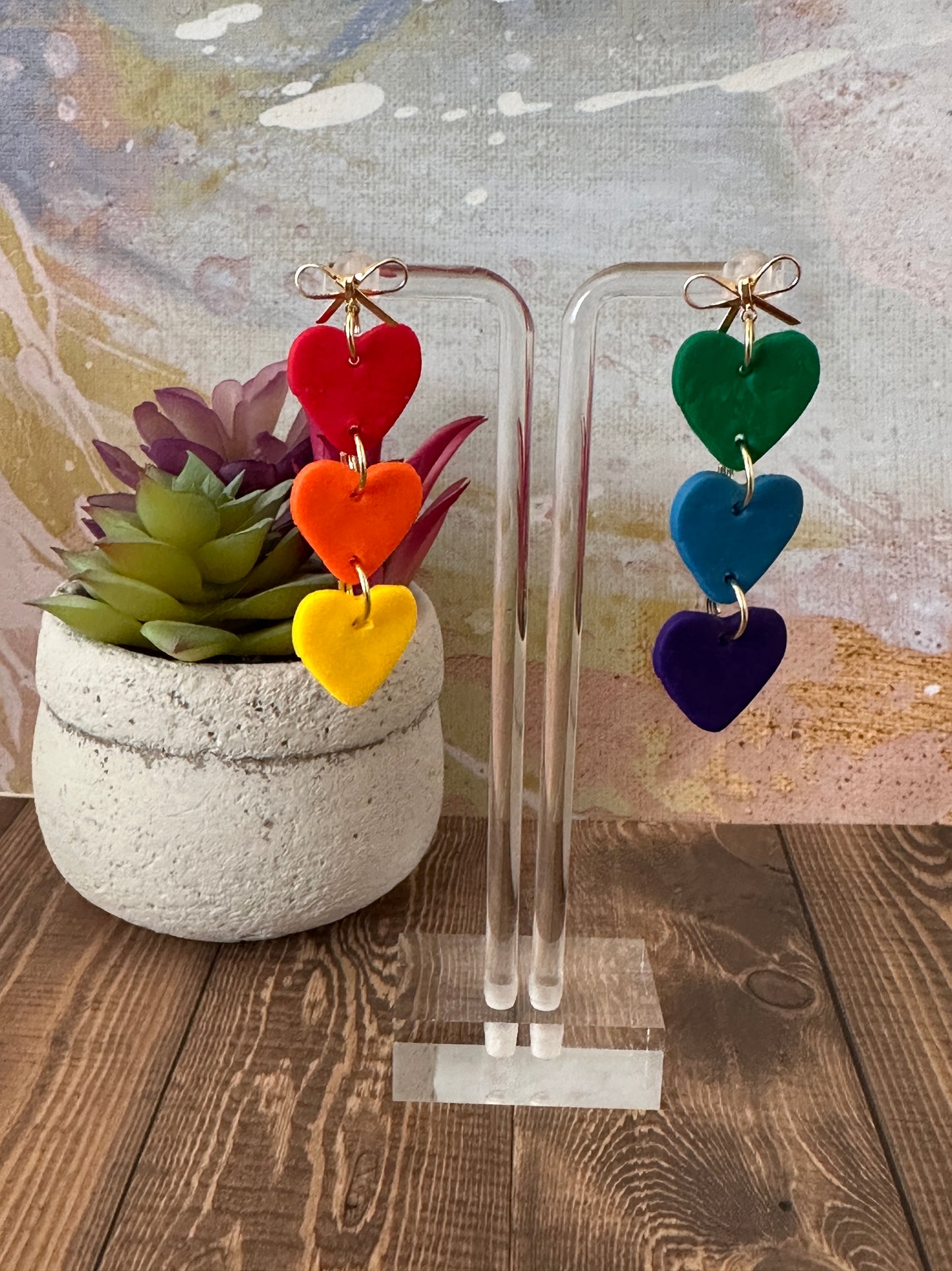 Colorful heart-shaped earrings on a stand with a potted plant in the background.