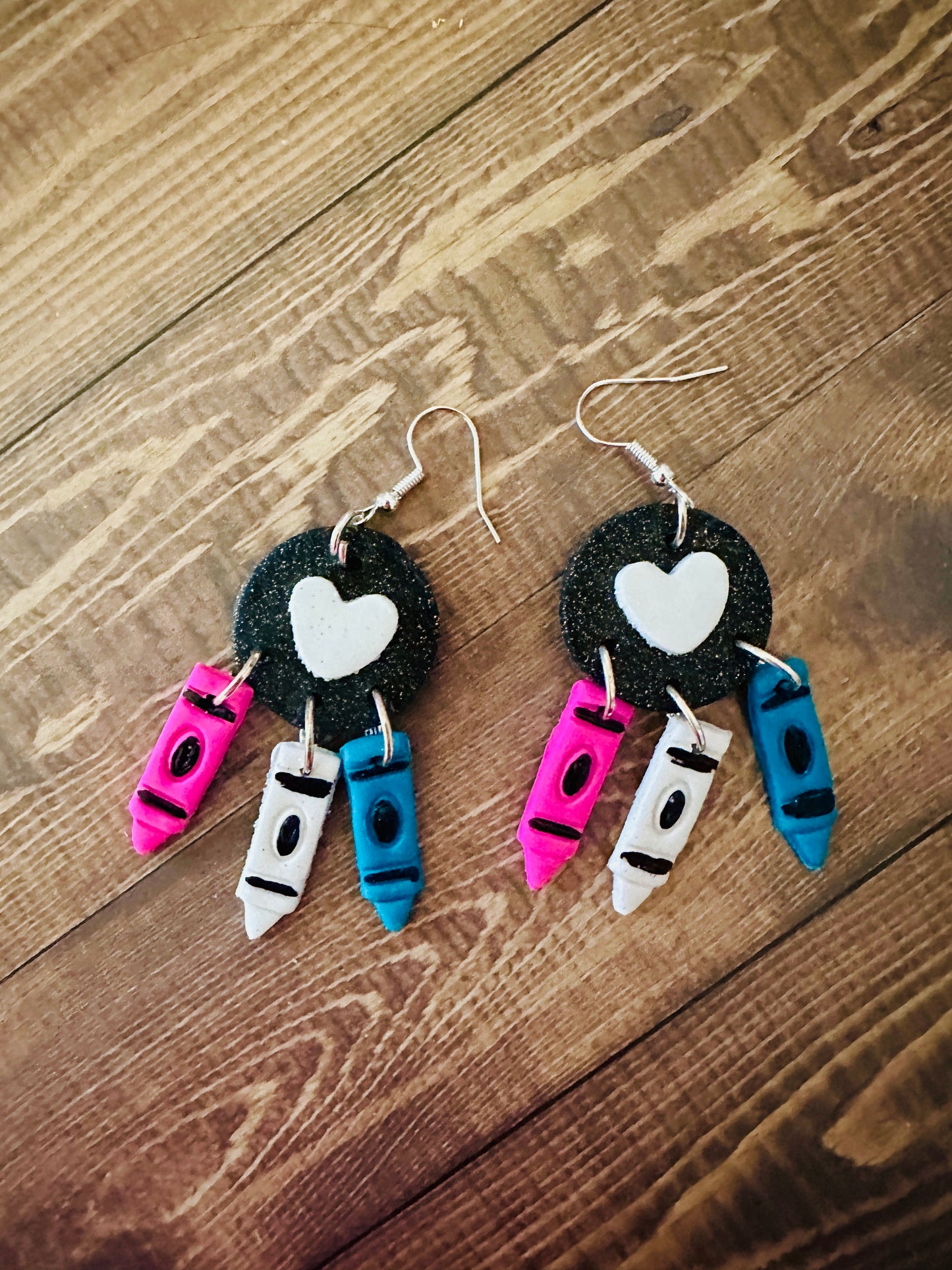 Handcrafted teacher crayon earrings on dark wooden table, lightweight polymer clay with nickel-free hooks, back to school.