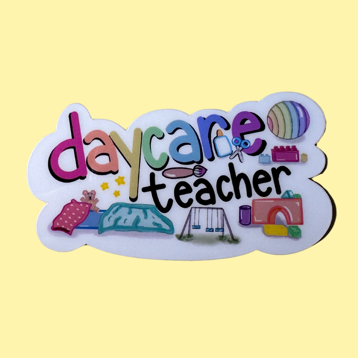 A die-cut sticker or patch with the words 'daycare teacher' in colorful playful lettering, decorated with small illustrations of toys and school items, shown on a solid pale yellow background.