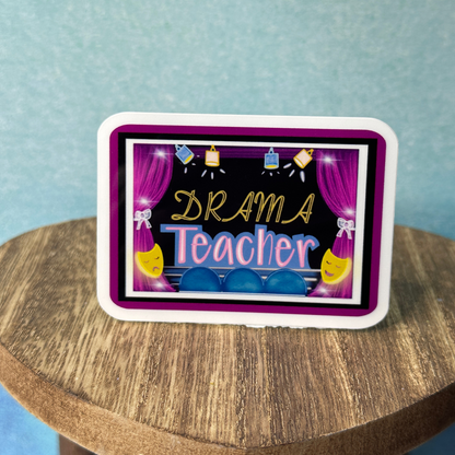 Drama teacher sticker displayed on wooden stand against light blue wall.