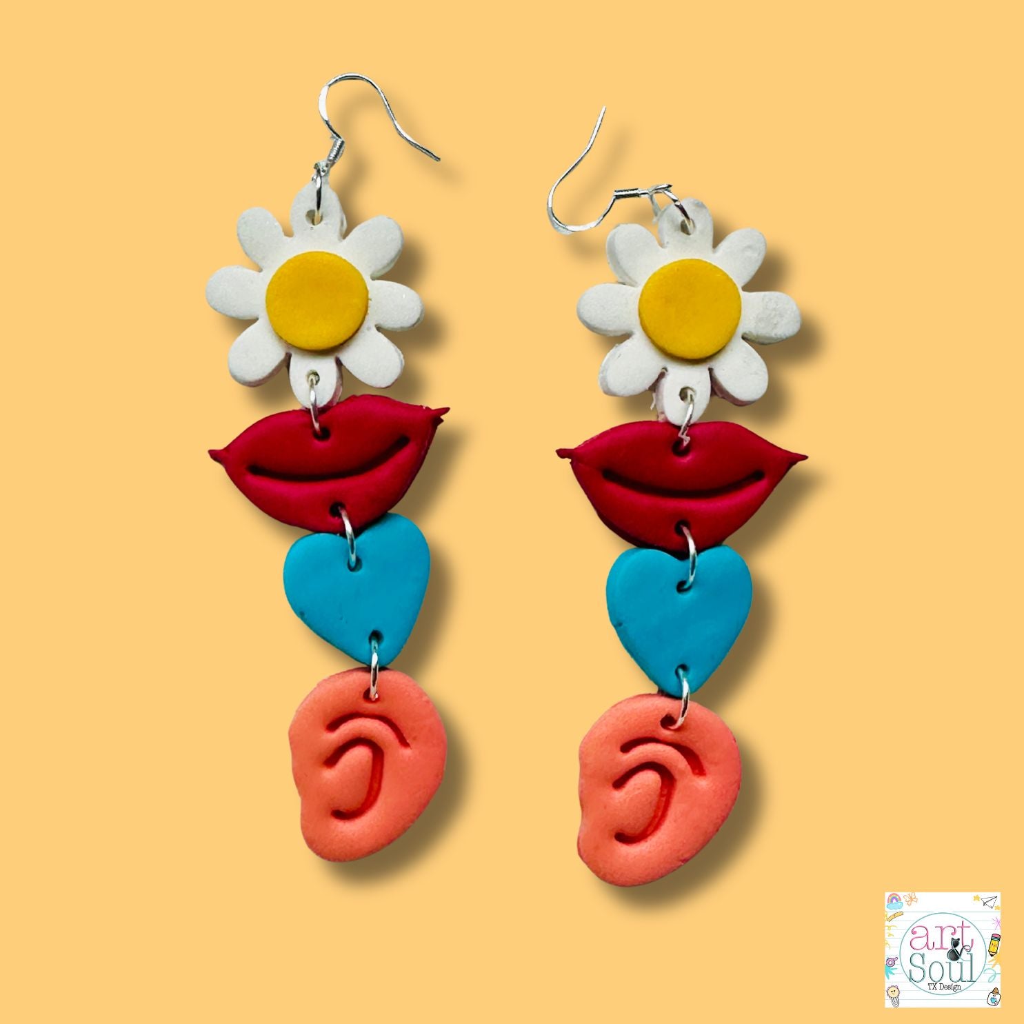 Colorful earrings with floral, lip, heart, and ear designs on a orange background.