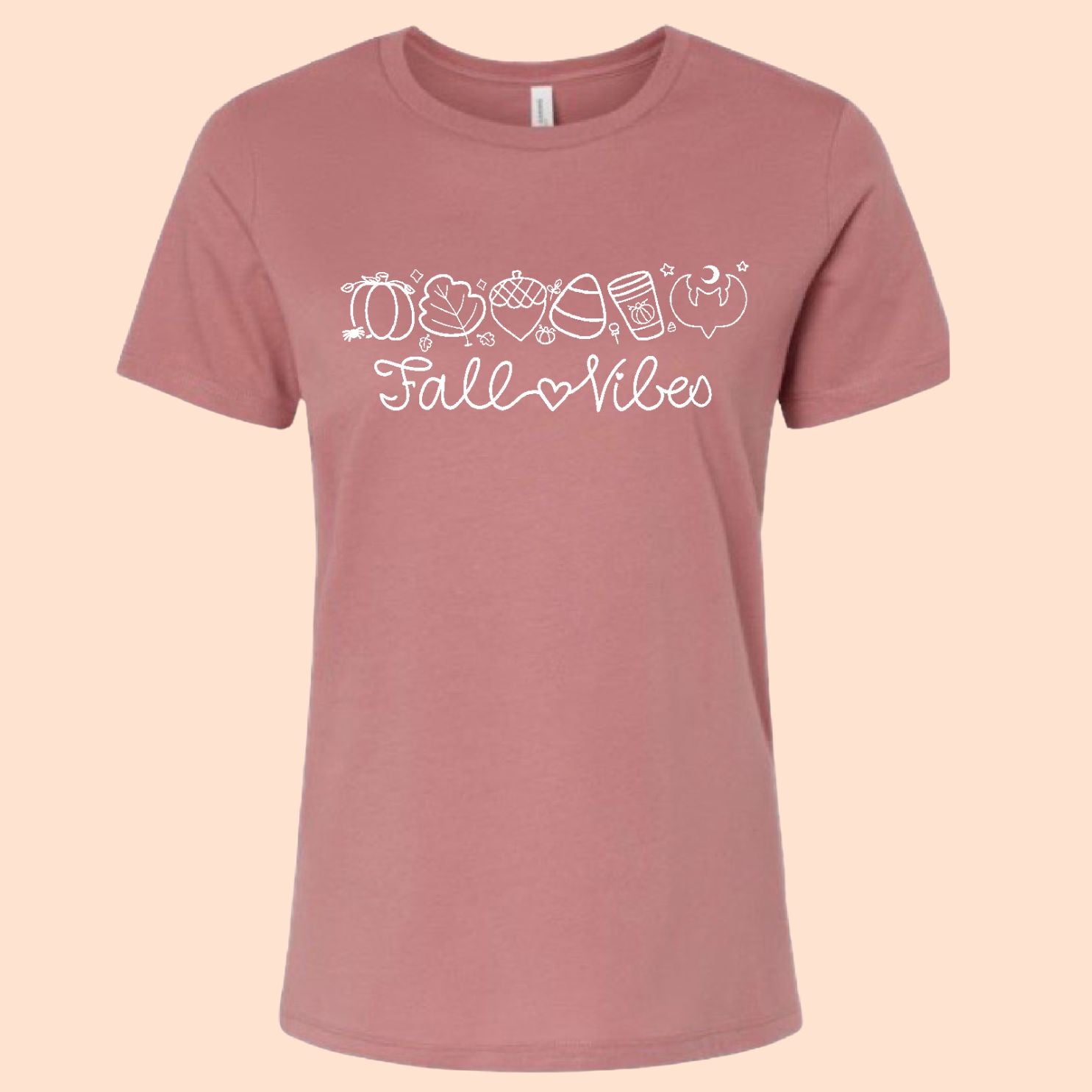 A dusty rose short-sleeve t-shirt with a white graphic print that reads 'Fall Vibes' with autumn-themed icons, displayed against a solid pale peach background.