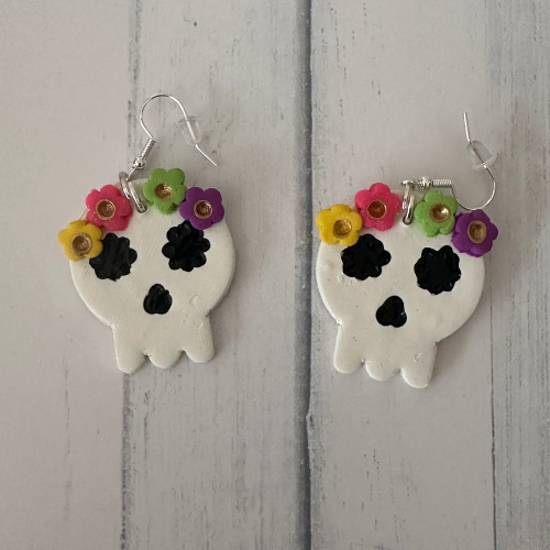 Handcrafted sugar skull polymer clay earrings with flower crown on white wood table, lightweight teacher Halloween jewelry