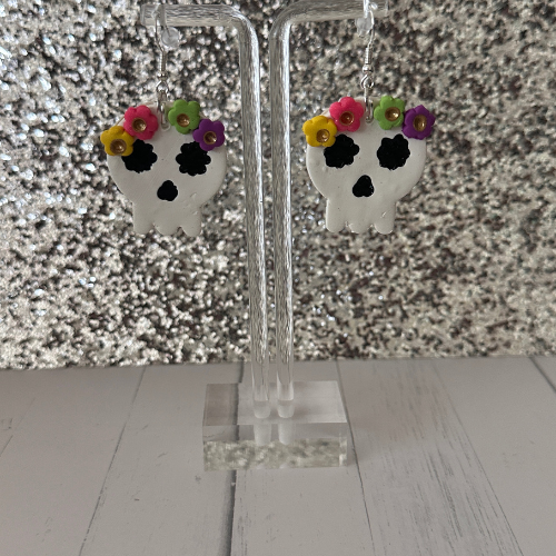 Dia de los Muertos flowery skull polymer clay earrings hanging on earring stand with glittery white background, teacher gift