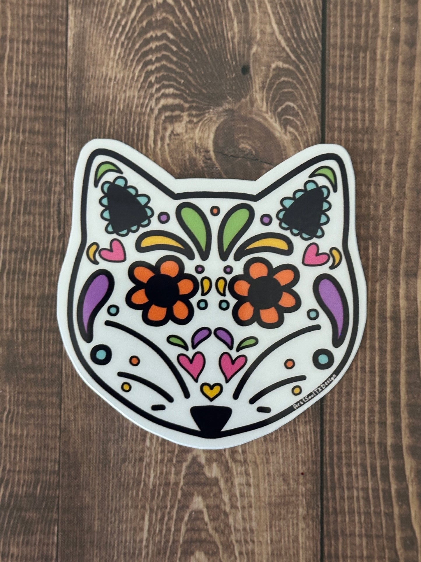 Hand-drawn fox sugar skull sticker on dark wood table, waterproof vinyl with colorful Dia de los Muertos patterns.