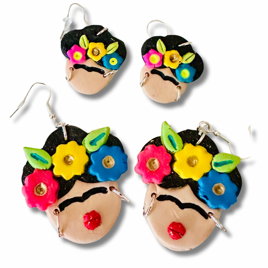 A comparison of the large and small variants on a white background.  The small size is displayed on top and has a simple face design with no red lips.  The larger variant is on the bottom and cute bright red lips.  Both have a three bright and vibrant flowers on Frida's forehead.