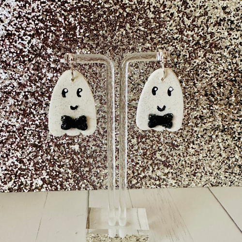 Cute ghost earrings hanging on stand with pink glittery backdrop, handcrafted polymer clay Halloween teacher jewelry gift.