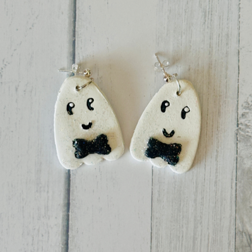 Handmade friendly ghost polymer clay earrings on white wooden table with bowties, hand-drawn details, Halloween teacher gift.
