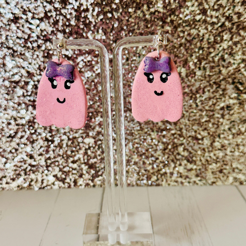 Cute pink ghost earrings hanging on stand with pink glittery backdrop, handcrafted polymer clay Halloween teacher jewelry gift.